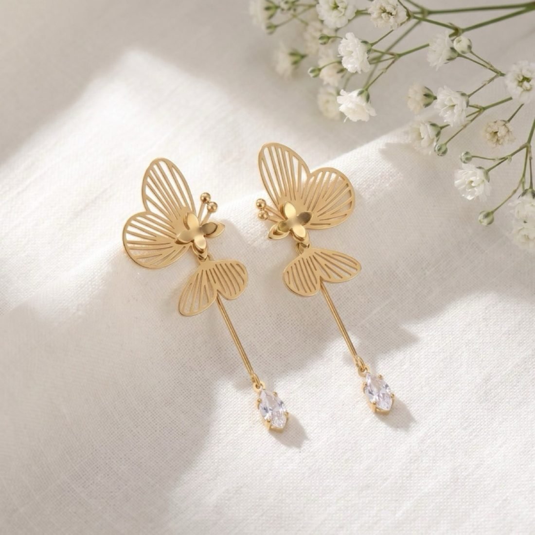 Luxury editorial campaign shot of gold butterfly earrings styled on white linen